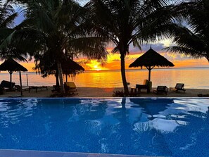 A poolside view with a sunset over the ocean, palm trees, and lounge chairs. -  Superior Oceanview Suite - Sleeps 5 Guests (Nungwi)