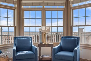 A room with two blue armchairs, a wooden side table, and a view of the city through large windows.
