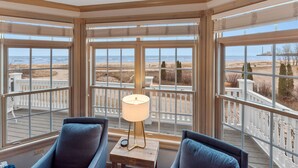 A corner room with large windows overlooking a beach, a small table with a lamp, and two chairs. - Beach front luxury spacious villa ! (Sheboygan)