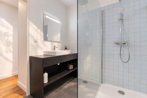 A modern bathroom with a glass-enclosed shower, a dark vanity with a mirror, and a white sink. - Charming and radiant flat of 55 m² located in the heart of Bordeaux (Bordeaux)