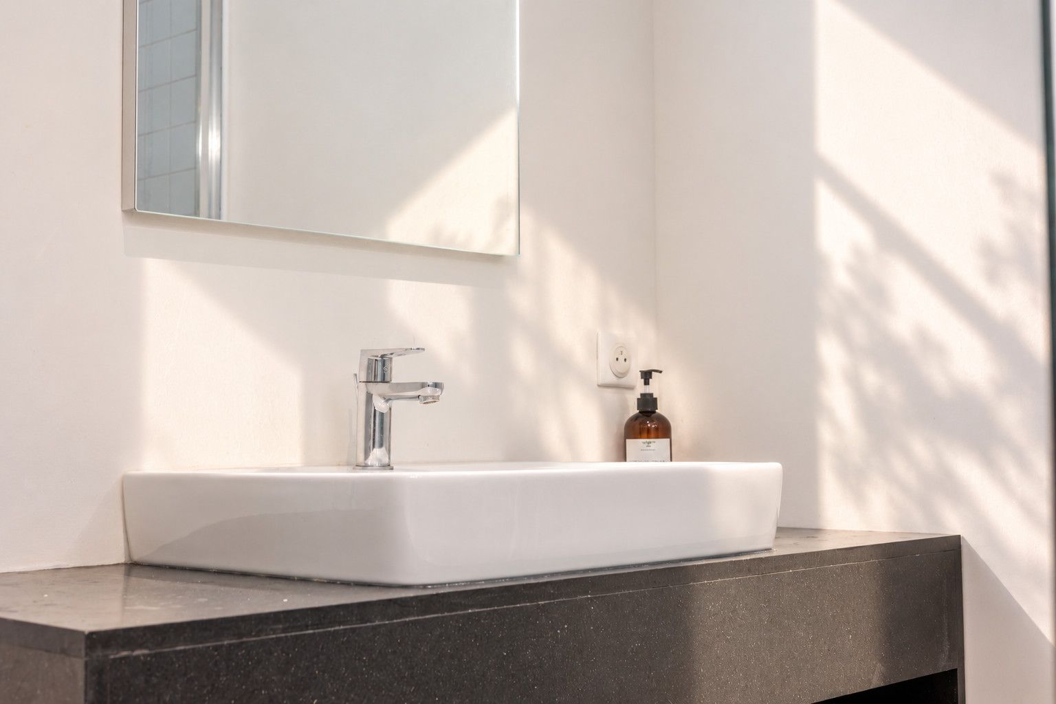 A bathroom with a white sink, a chrome faucet, and a bottle of soap on the counter.