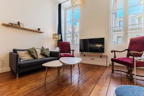 Un salon comprenant un canapé, deux fauteuils, une petite table, un téléviseur et une bibliothèque.