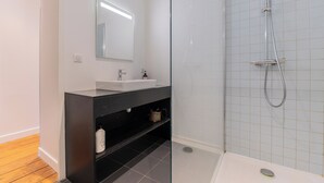 Een moderne badkamer met een douchecabine van glas, een witte wastafel en een donkere badkamerkast.