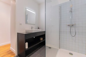 A modern bathroom with a glass-enclosed shower, a white sink, and a dark vanity.