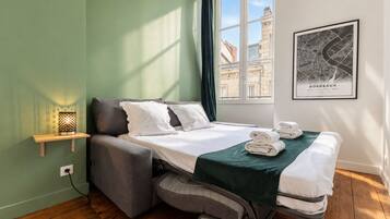 Quarto de hotel compacto com cama, mesa de cabeceira com abajur, janela com vista para edifícios e um mapa emoldurado na parede.