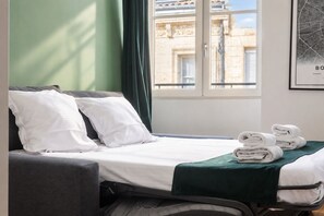 A hotel room with a bed, pillows, a green blanket, and a window with a view of a building.