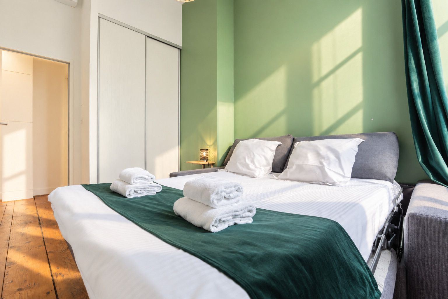 Habitación de hotel con cama, mesita de noche, lámpara y vistas al exterior.