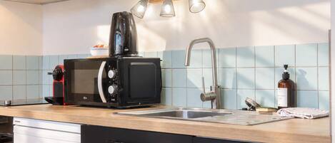 A modern kitchen with a built-in microwave, a coffee maker, a sink, and a wooden countertop.