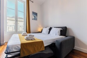 Een hotelkamer met een bed, een slaapbank, een raam met gordijnen en een poster aan de muur.