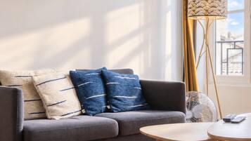 A modern living room with a sofa, two pillows, a floor lamp, a side table, and a remote control.