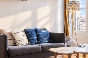 Ein modernes Wohnzimmer mit einer Couch, zwei Kissen, einer Stehlampe, einem Beistelltisch und einer Fernbedienung.