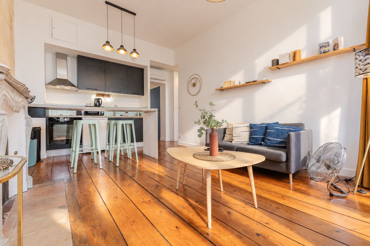 Una cocina moderna con taburetes de bar, una mesa de comedor y un área de estar con sofá y ventilador.