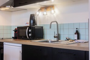 Een moderne keuken met een ingebouwde magnetron, koffiezetapparaat, spoelbak en een houten aanrecht.