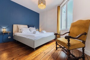 Une chambre à coucher avec un lit, une chaise, une table de chevet avec une lampe et une fenêtre.