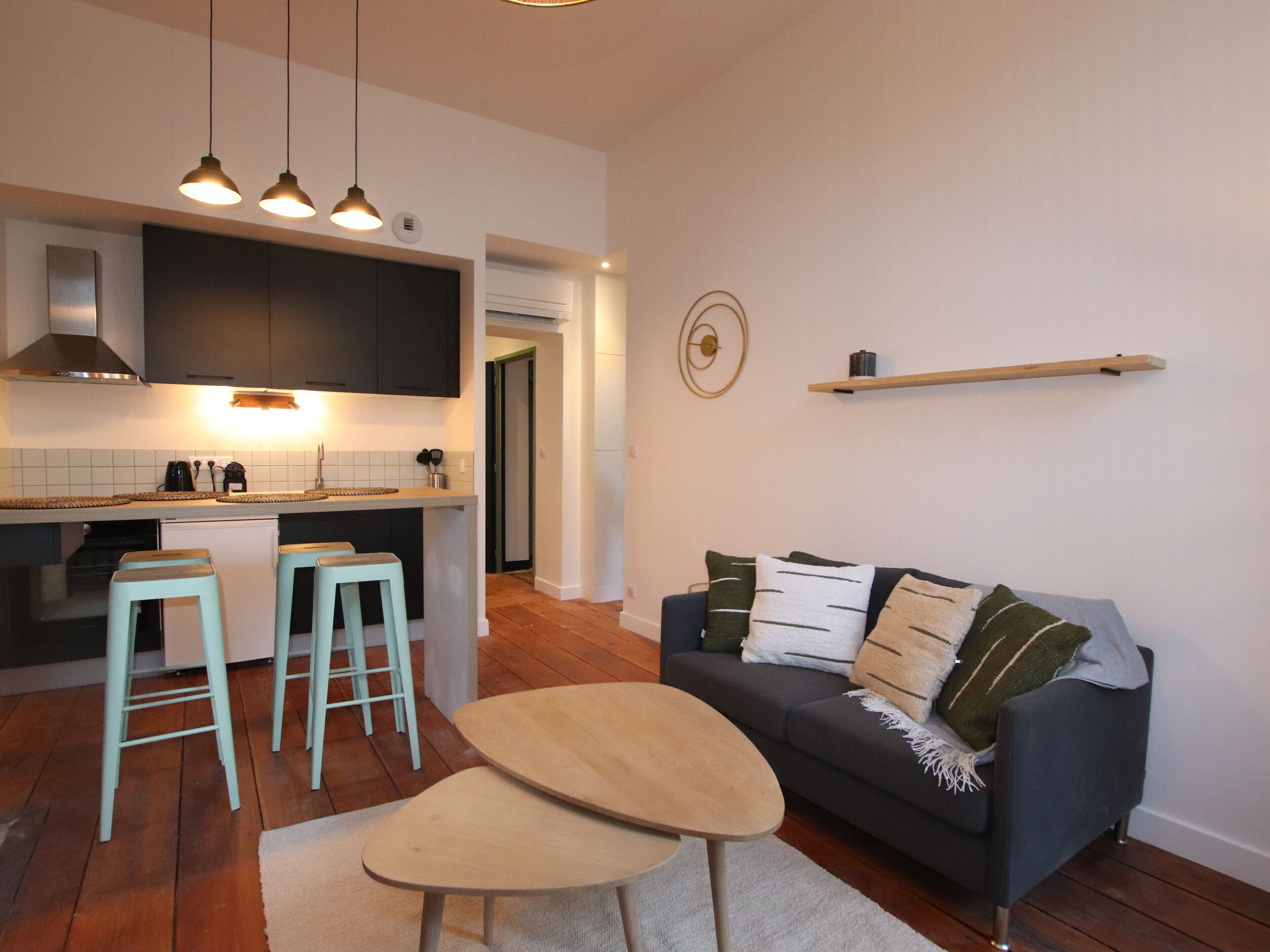 Een moderne keuken met een centraal eiland, barstoelen, een donkergrijze bank met kussens en een houten salontafel.