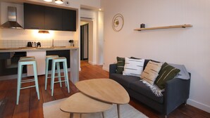 Eine moderne Küche mit Kochinsel, Barhocker, einem dunkelgrauen Sofa mit Kissen und einem Holztisch.