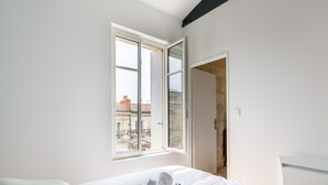 A bedroom with a bed, a window, and a door leading to another room.