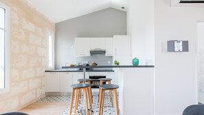 A modern kitchen with white cabinets, a black countertop, and a built-in oven. There are three stools with wooden legs and metal bases. The kitchen has a large window and a small island with a sink.