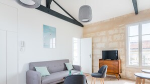 A modern living room with a grey sofa, two chairs, a wooden cabinet with a TV, and a large window. - Superb flat in the heart of the Chartrons, renovated, spacious and bright (Bordeaux)
