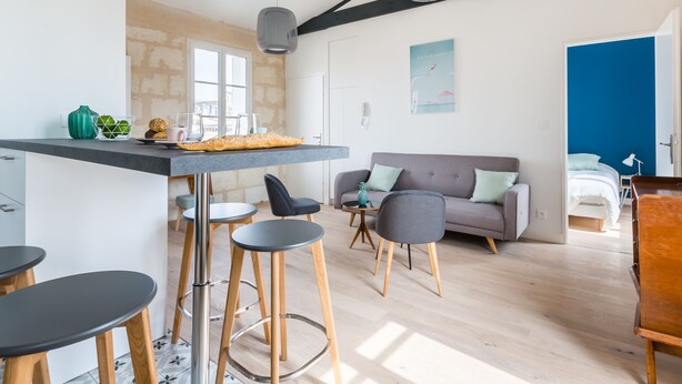 A modern living room with a sofa, chairs, a dining table, and a kitchen area with a window. - Superb flat in the heart of the Chartrons, renovated, spacious and bright (Bordeaux)