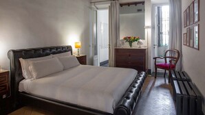 A bedroom with a large bed, a bedside table with a lamp, a dresser, a chair, and a mirror on the wall. - ROMAC Leone V Unique 5-bdr near the Spanish Steps (Roma)