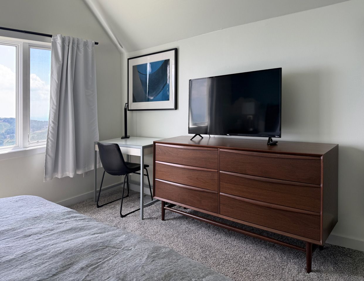 A hotel room with a bed, a desk, a dresser, a television, and a window with curtains.