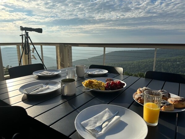 A table set with breakfast plates, a telescope, and a scenic view.