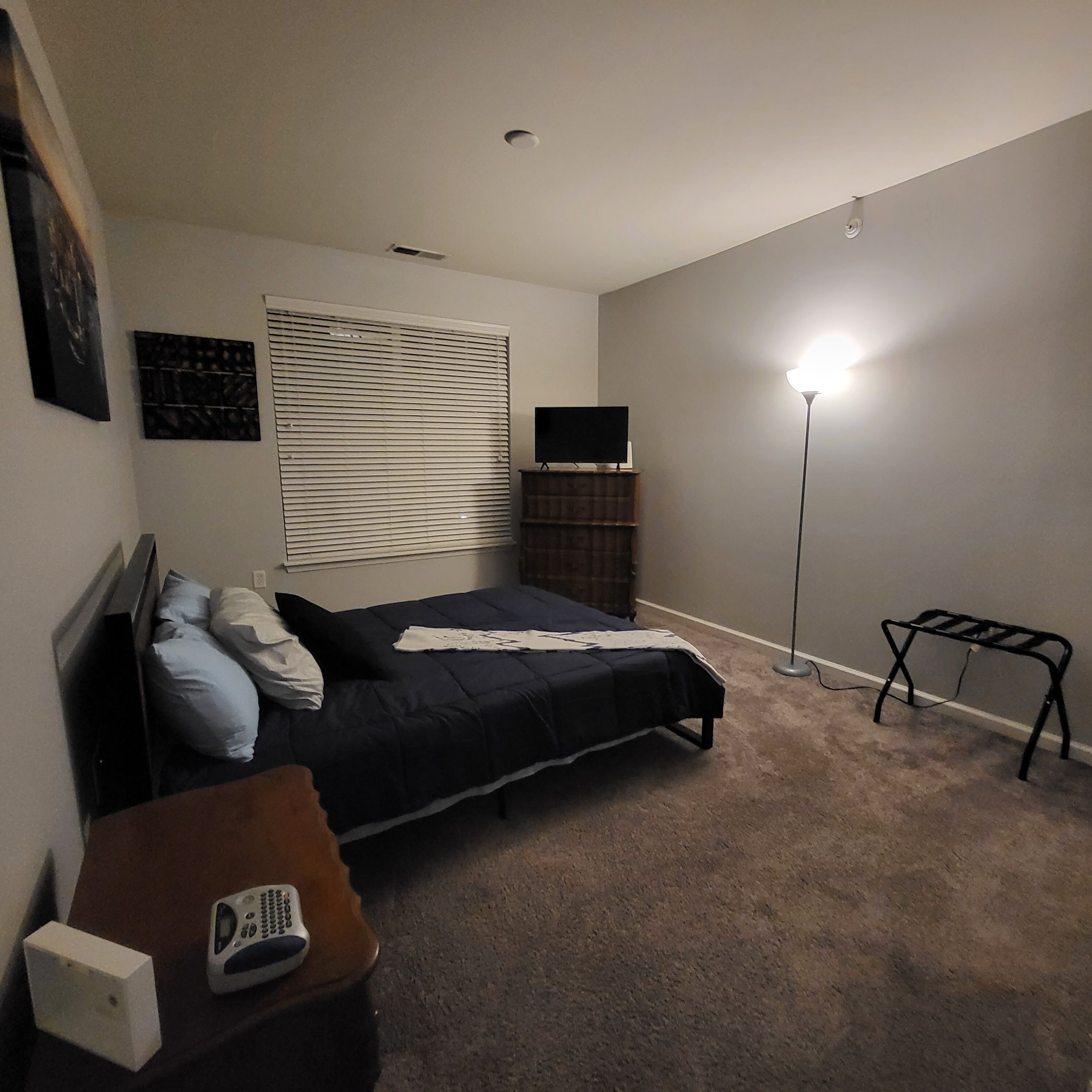 Una camera da letto con un letto, un comodino, una lampada, una TV su un mobile e una finestra con persiane.