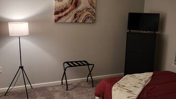 A bedroom with a bed, a floor lamp, a black chair, a TV on a stand, and a marble-patterned artwork on the wall.