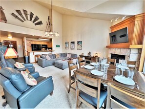 A spacious living room with a sectional sofa, a dining table set for four, and a kitchen in the background.
