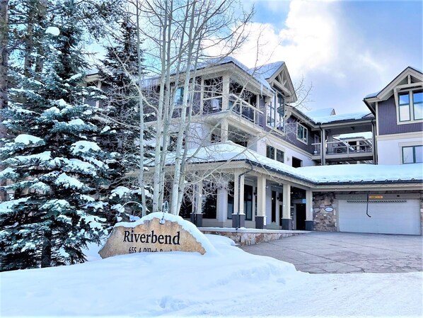 A multi-story hotel with a snow-covered landscape, a prominent 'Riverbend' sign, and a large driveway. - Riverbend Liftside Condo • Ski In/Out • Snowflake Lift • Pool+Hot Tub (Breckenridge)