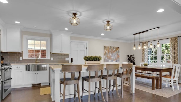 A modern kitchen with white cabinetry, a dining area with wooden chairs, and pendant lighting.
