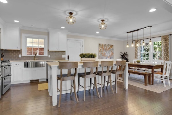 A modern kitchen with white cabinetry, a dining area with wooden chairs, and pendant lighting.