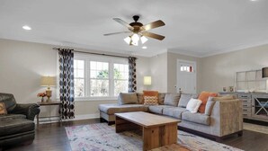 A living room with a sectional sofa, a coffee table, a ceiling fan, and a window with patterned curtains.