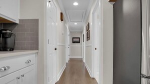 A narrow hallway with white cabinetry, a coffee maker on the left, and a refrigerator on the right.