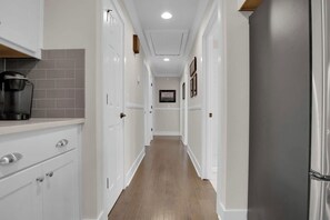 A narrow hallway with white cabinetry, a coffee maker on the left, and a refrigerator on the right.