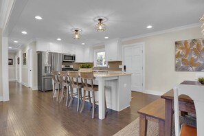 A modern kitchen with white cabinetry, stainless steel appliances, and a central island with bar stools. - Tiger Walk - 3 Miles from Death Valley! (Clemson)