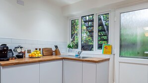 A modern kitchen with white cabinets, a wooden countertop, a coffee maker, a fruit bowl, and a window with a view of greenery. - Stunning 2-Bed Apartment in Purley - Croydon Gem (Purley)