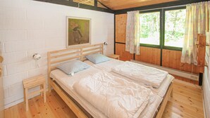 Quarto com duas camas de solteiro, cabeceira de madeira, mesa de cabeceira pequena, luminária acoplada à parede e janela com cortinas.