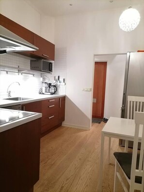 Cocina compacta con armarios de madera, un microondas y un lavamanos. Hay una mesa de comedor blanca con sillas.