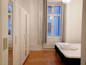 Un dormitorio con cama, ventana con cortinas, armario y radiador.