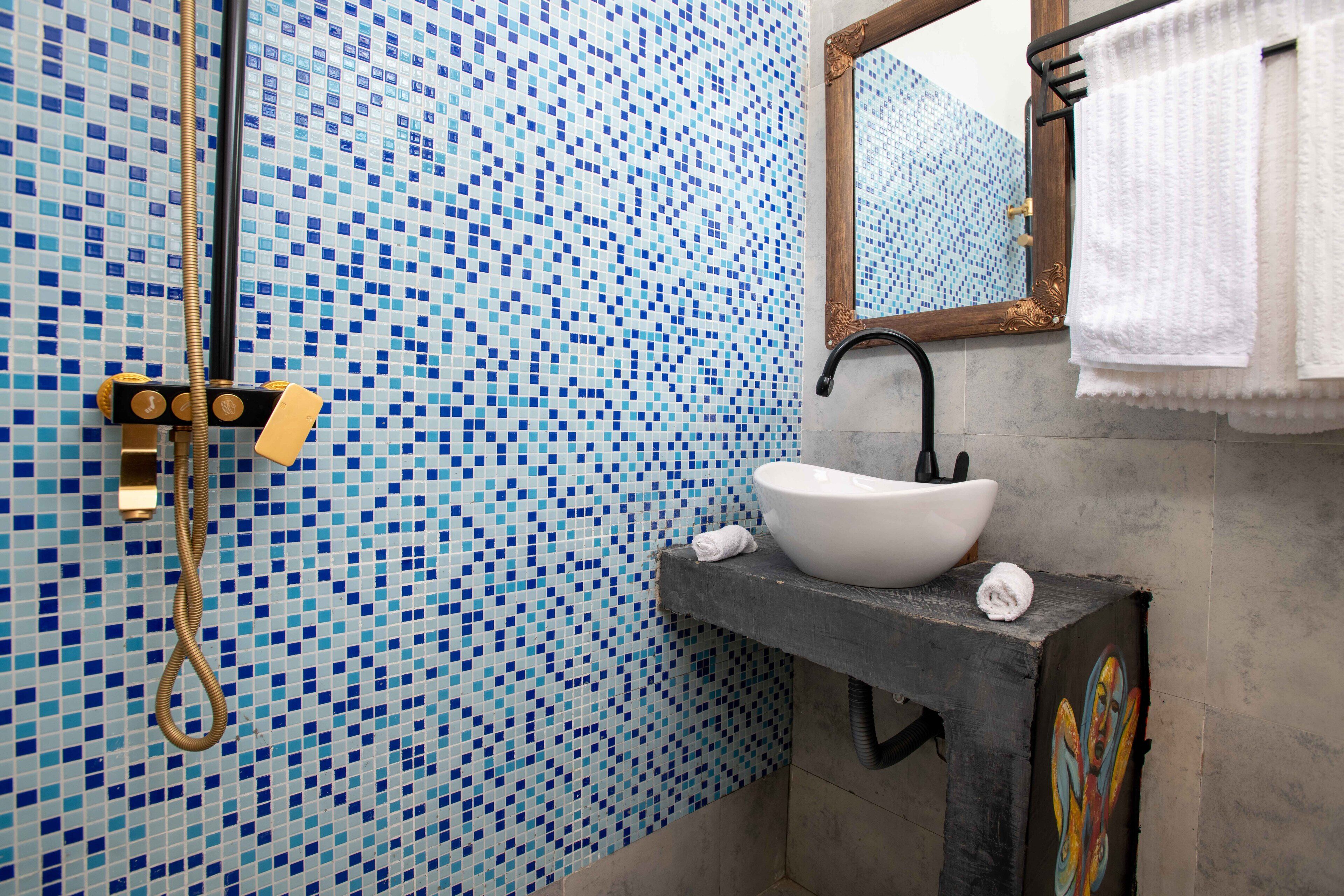 A bathroom with a mosaic tile wall, a white sink, a mirror, and a towel rack.