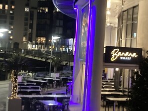 Un espacio al aire libre con mesas y sillas, un letrero que dice 'Banana Wharf' y un edificio al fondo.
