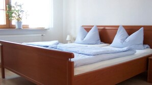 A single bed with a wooden frame, a white mattress, and light blue bedding. There is a bedside table with a lamp, and a potted plant on the windowsill. - Vacation apartment with 50 square meters - at Gästehaus Kunz in Rust (Rust)