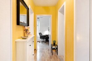 Un couloir avec une armoire blanche, un miroir, une plante en pot et une chaise.