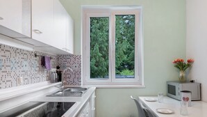A kitchen with a window, a microwave, a trash bin, and a table with a plate and a glass. - Apartment 'Amselnest' with Private Terrace, Private Garden (Kempten)