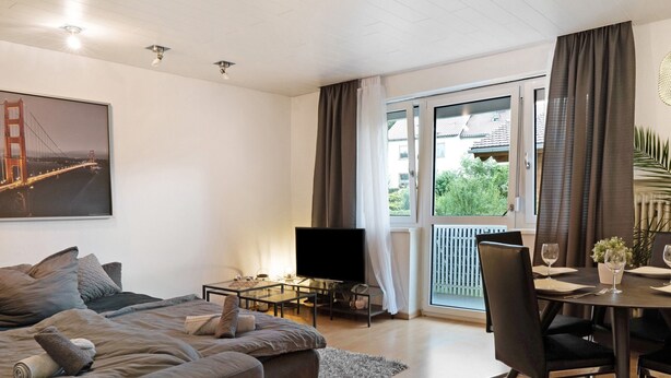 A modern living room with a sofa, TV, dining table, and a balcony with curtains. - Apartment 'Amselnest' with Private Terrace, Private Garden (Kempten)