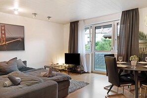 Un salon moderne comprenant un canapé, un téléviseur, une table à manger et un balcon agrémenté de rideaux.