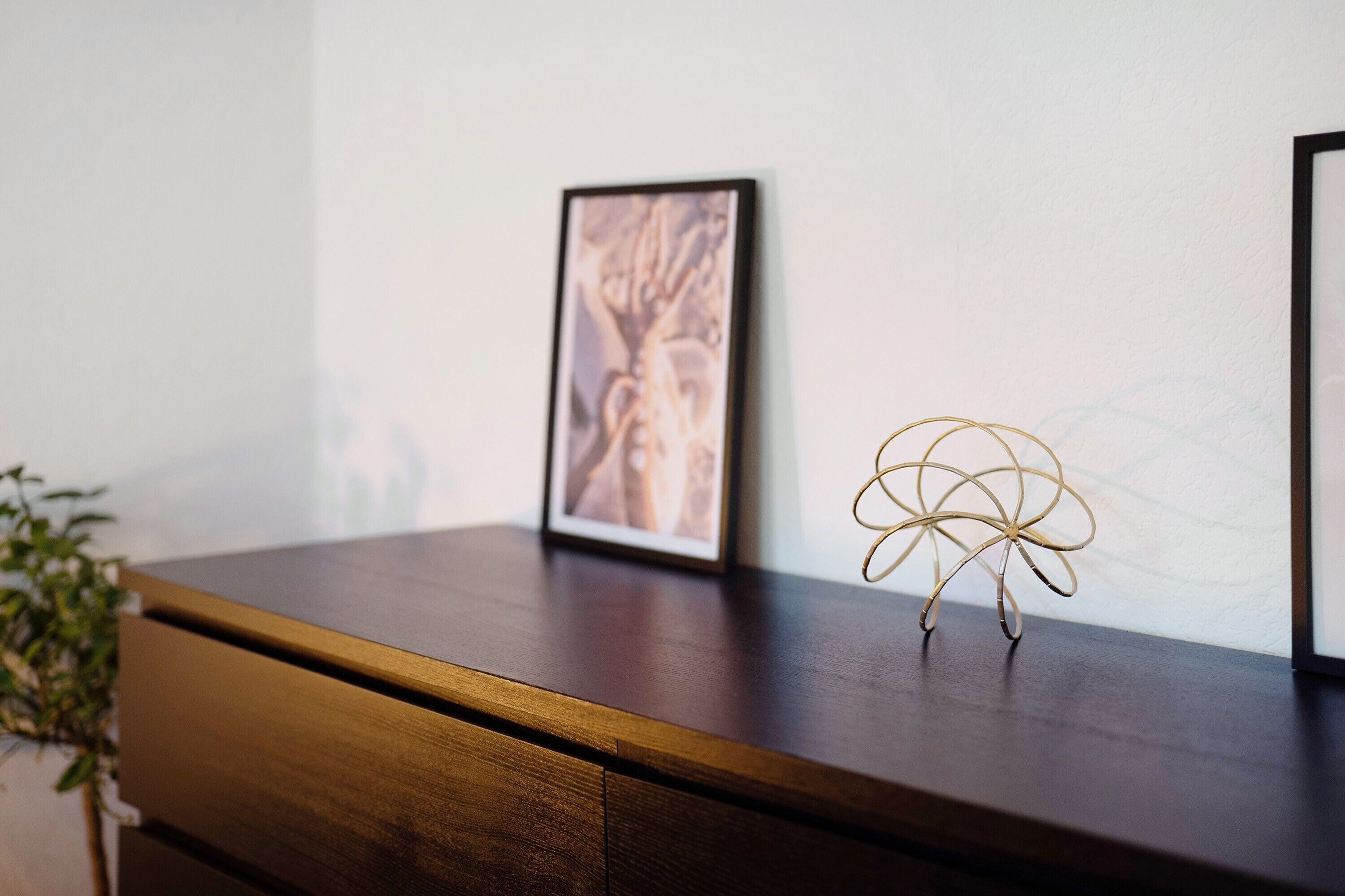 Uma cômoda de madeira com um quadro emoldurado e um objeto decorativo de arame em cima.