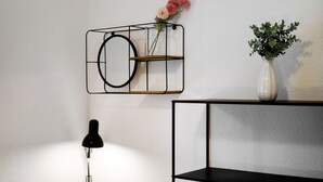 A wall-mounted shelf with a vase containing flowers, a black lamp, and a black shelving unit. - Apartment 'Amselnest' with Private Terrace, Private Garden (Kempten)